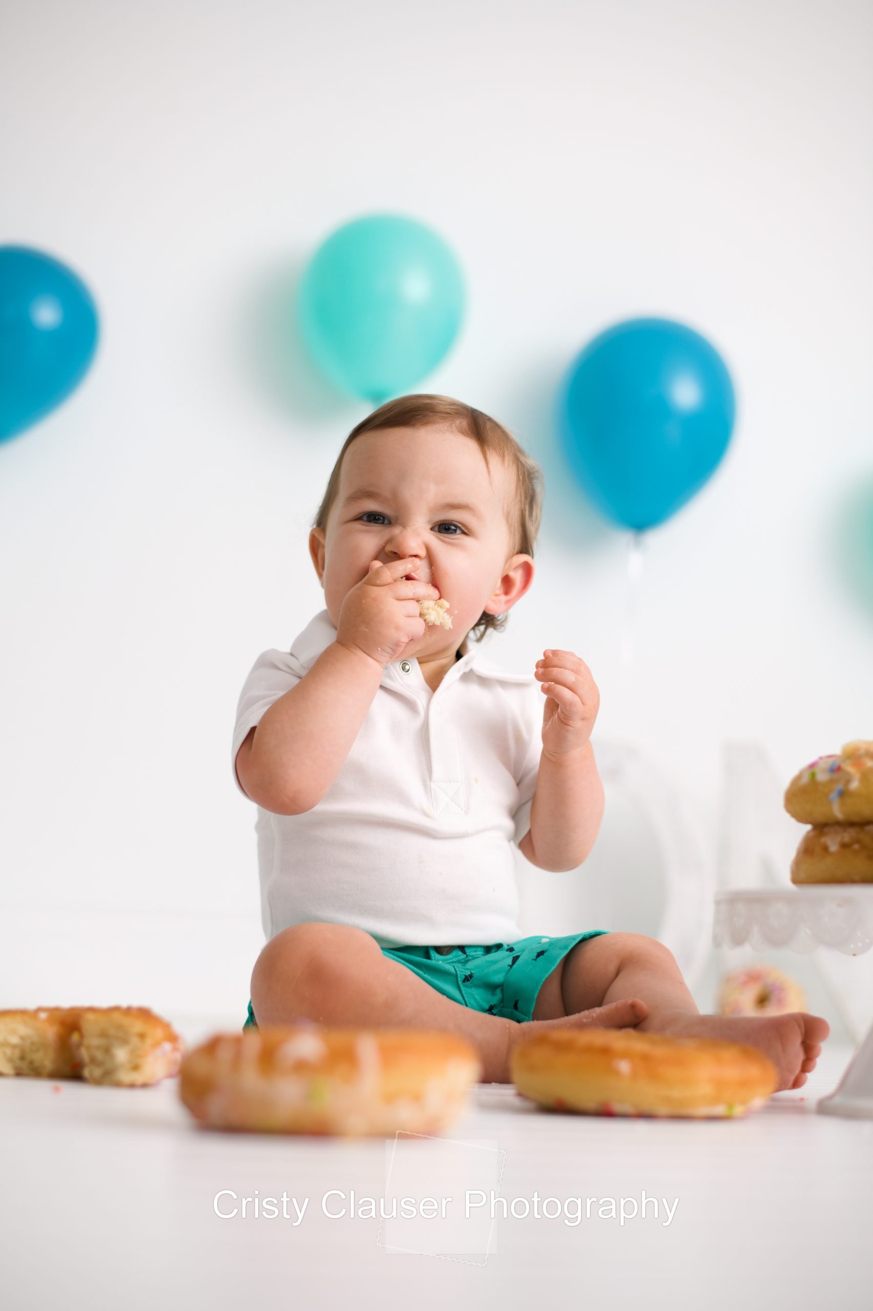 A baby's gaze meets the camera as they eagerly put a donut into their mouth.